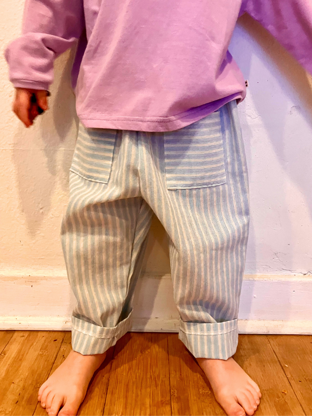 A child is wearing Pocket Stripe Pant cuffedwith a purple tee.