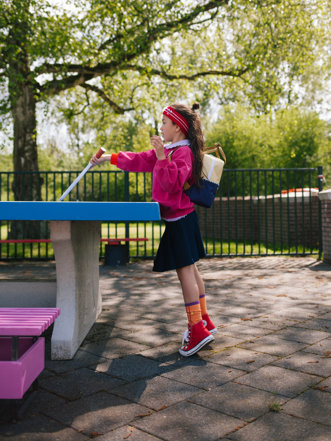 A child is wearing a colourblocking backpack in Feather Shuttle with a pink sweatshirt, playing a sport. 