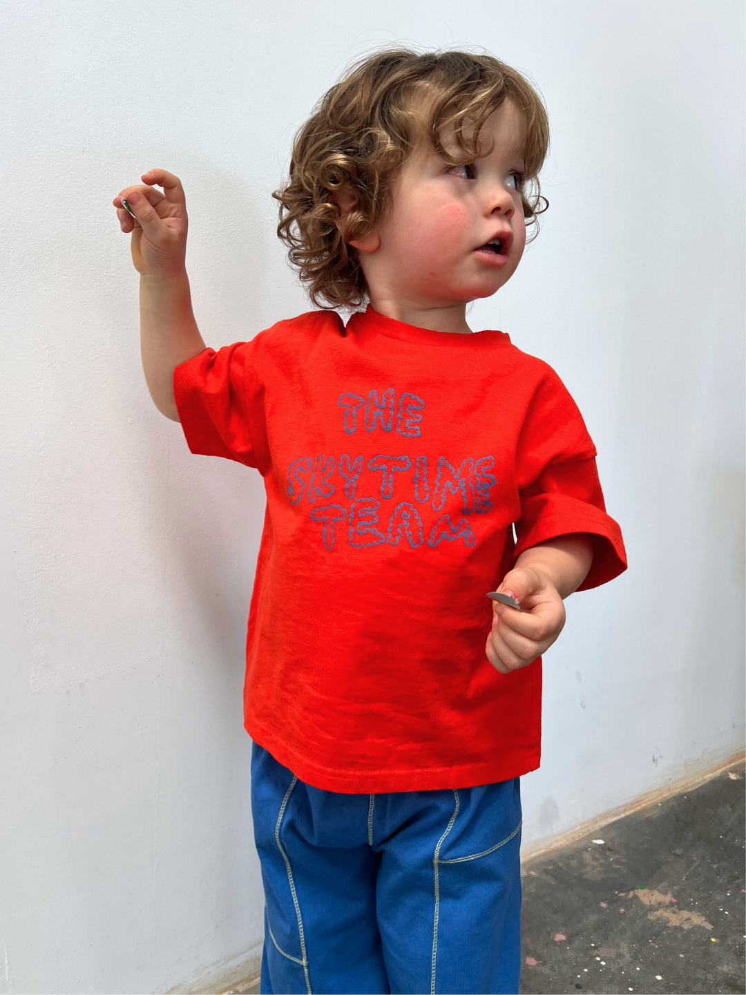 Red | Child wearing a red t-shirt with text against a white wall