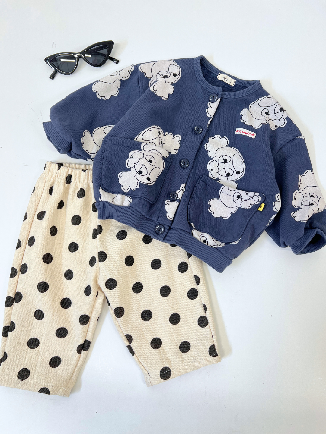 Navy | Children's outfit featuring a Poodle Button Down Sweatshirt in navy with cartoon elephants, beige pants with black polka dots, and black sunglasses on a white backdrop. Perfect for toddlers, this ensemble combines style and comfort with French terry elegance.