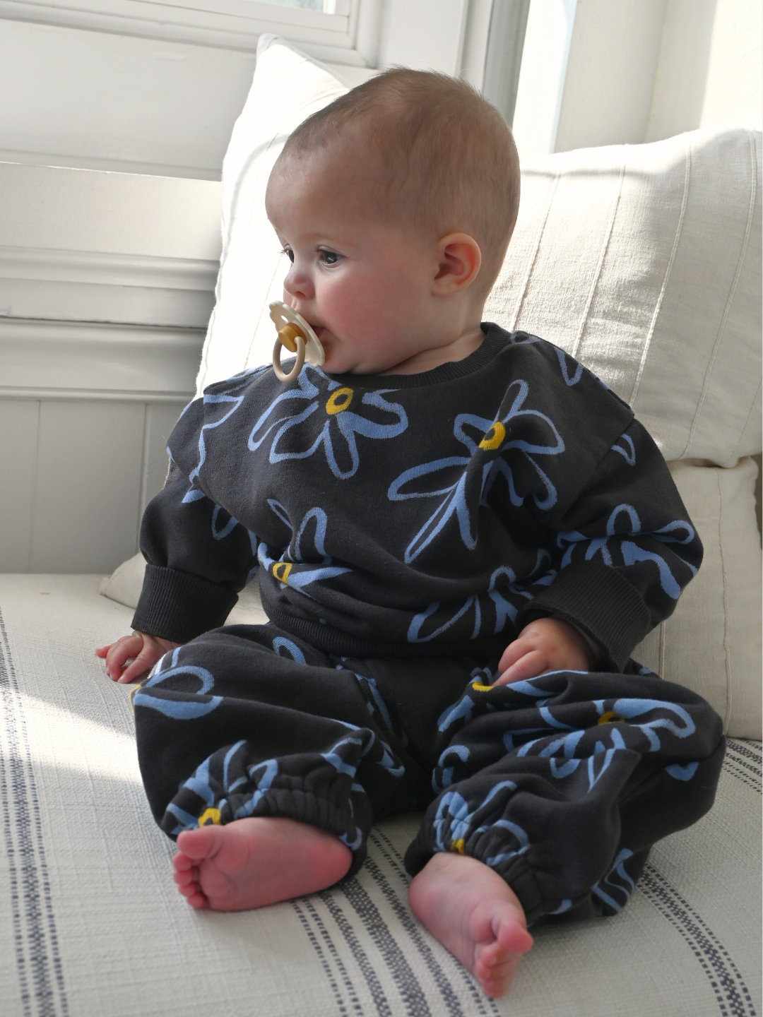 Charcoal | Baby wearing a black outfit with blue floral patterns sitting on a couch.