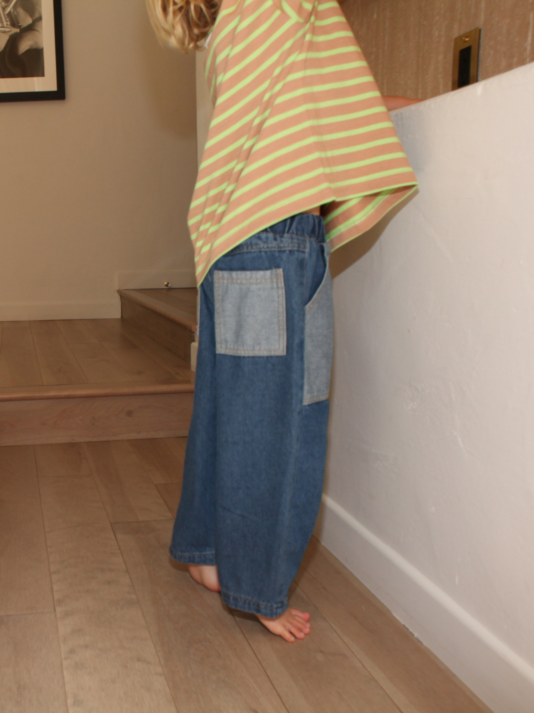 Dark Wash | A child wearing a striped shirt and denim pants standing on a wooden floor.