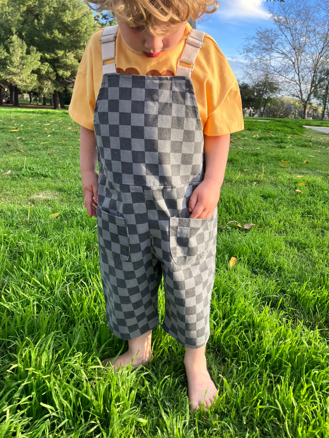 A child is wearing checker overalls in charcoal over a yellow tee