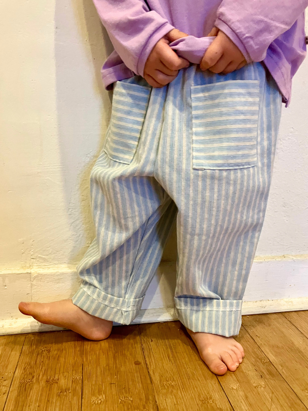 A child is wearing Pocket Stripe Pant cuffedwith a purple tee. 