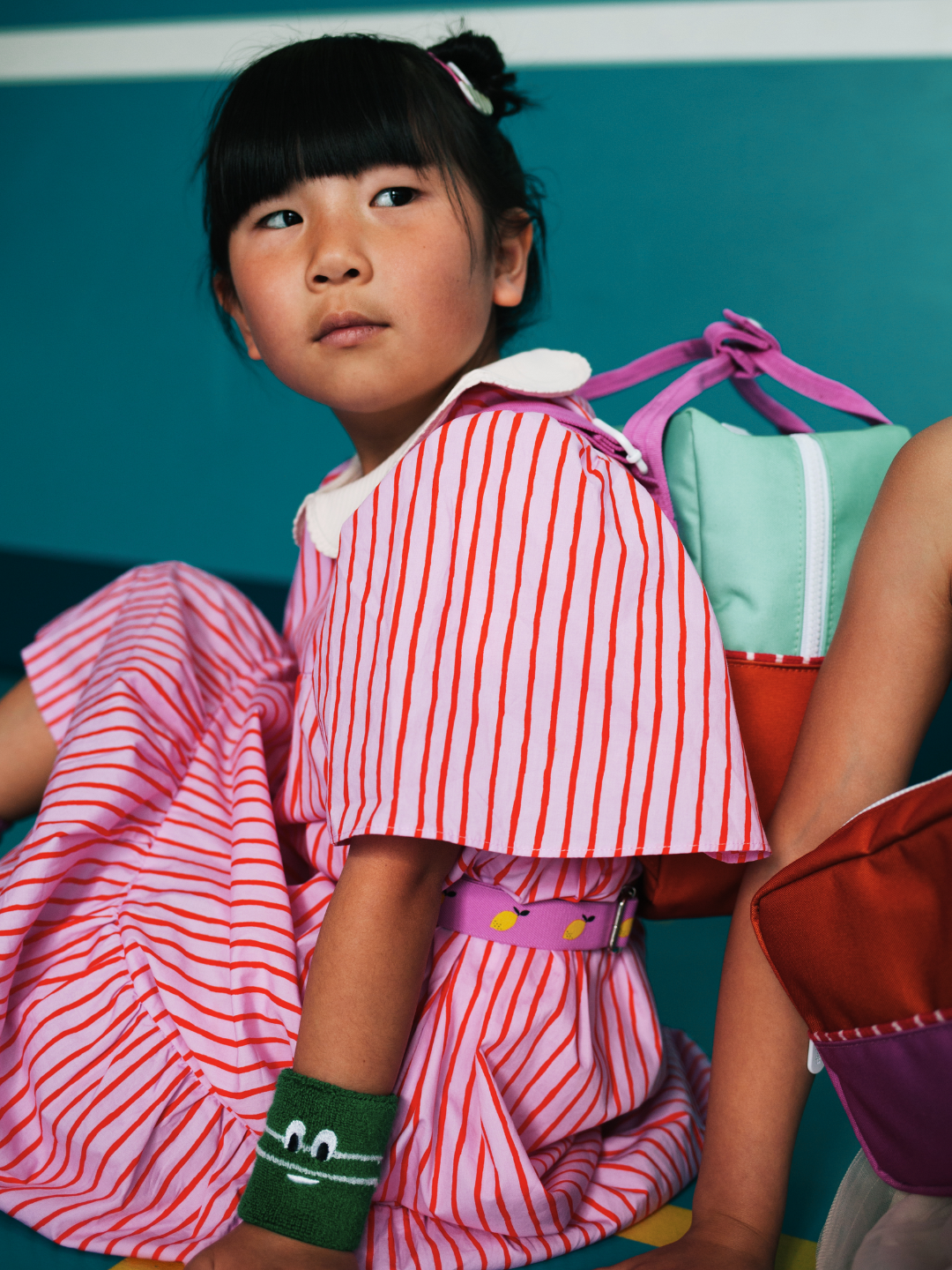 A child is wearing a colourblocking backpack in Towel Green with a stripe dress.