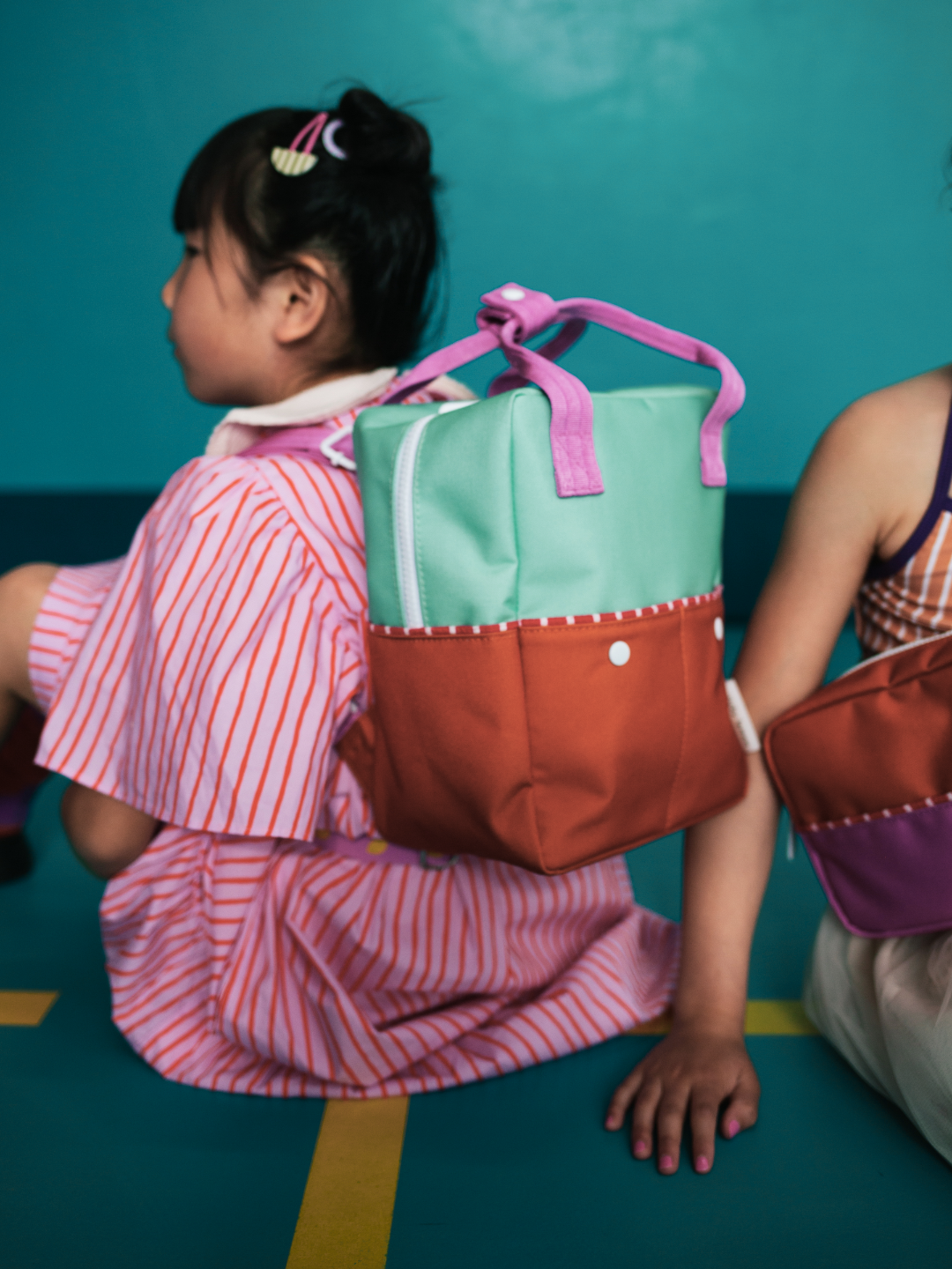 A child is wearing a colourblocking backpack in Towel Green with a stripe dress.