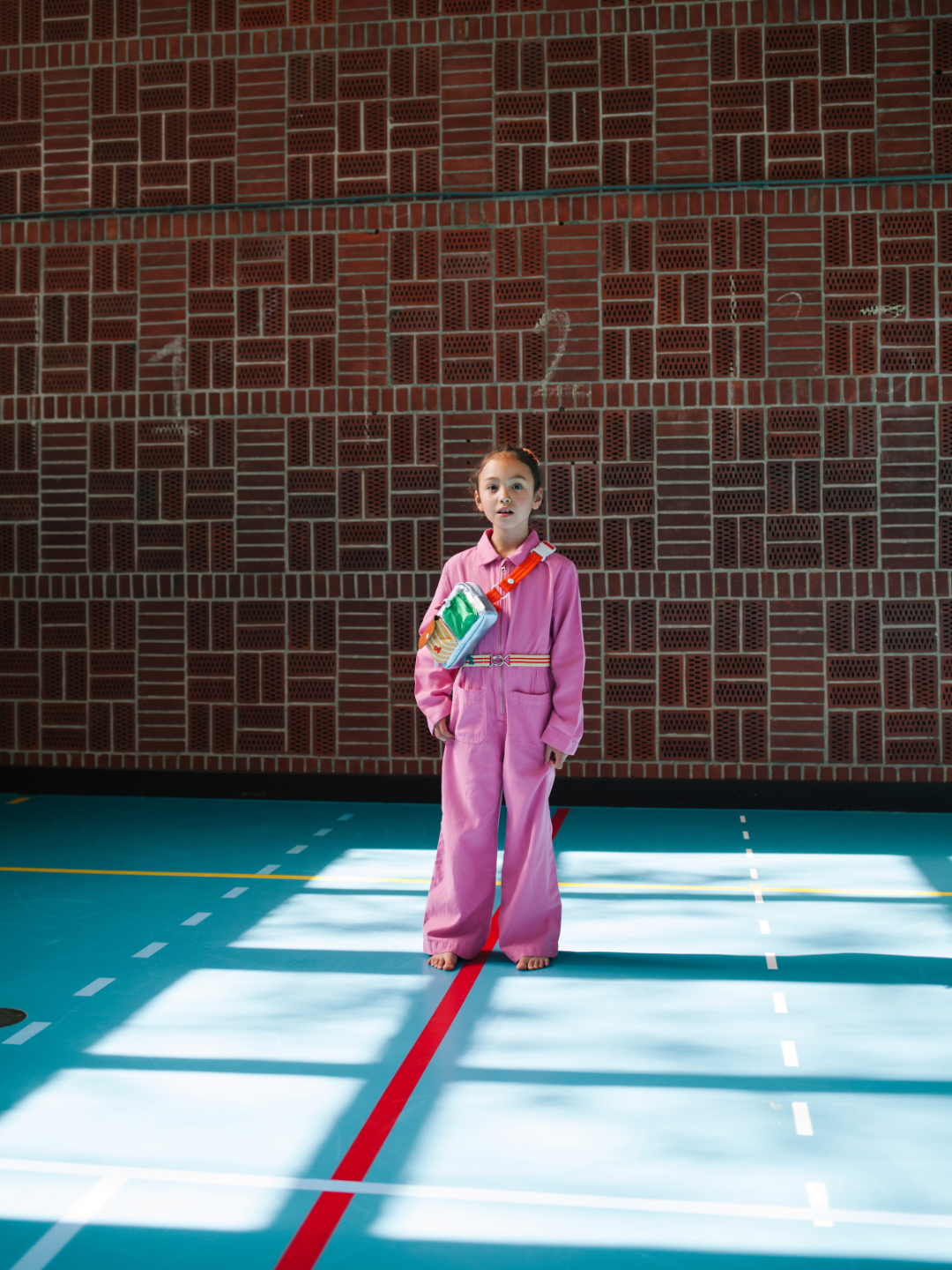 A child is wearing a Metallic Blue bike bag with a pink jumpsuit.