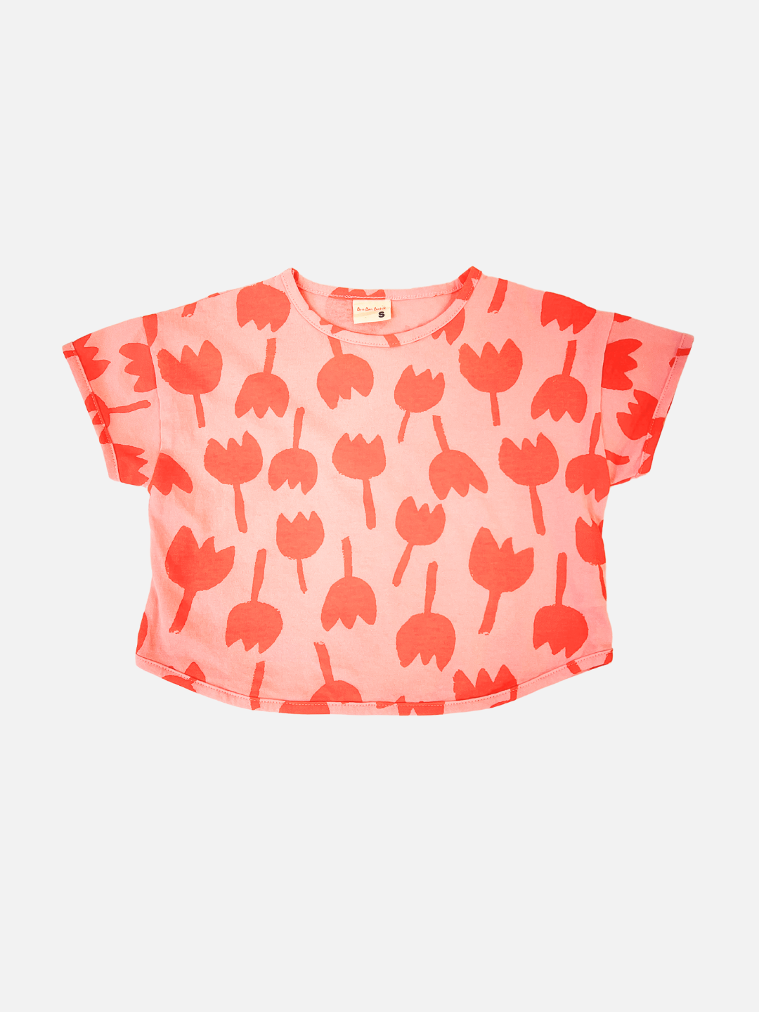 Front view of kids tulip tee with short sleeves in coral pink with an all-over print of dark pink graphic tulip shapes.