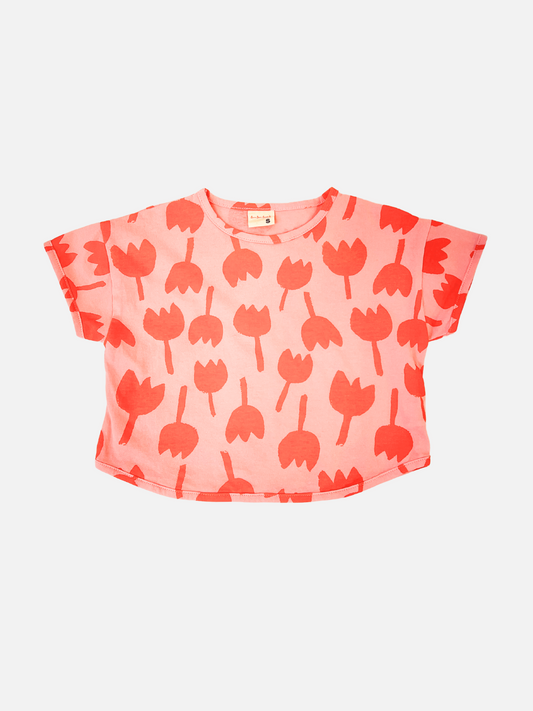 Image of Front view of kids tulip tee with short sleeves in coral pink with an all-over print of dark pink graphic tulip shapes.