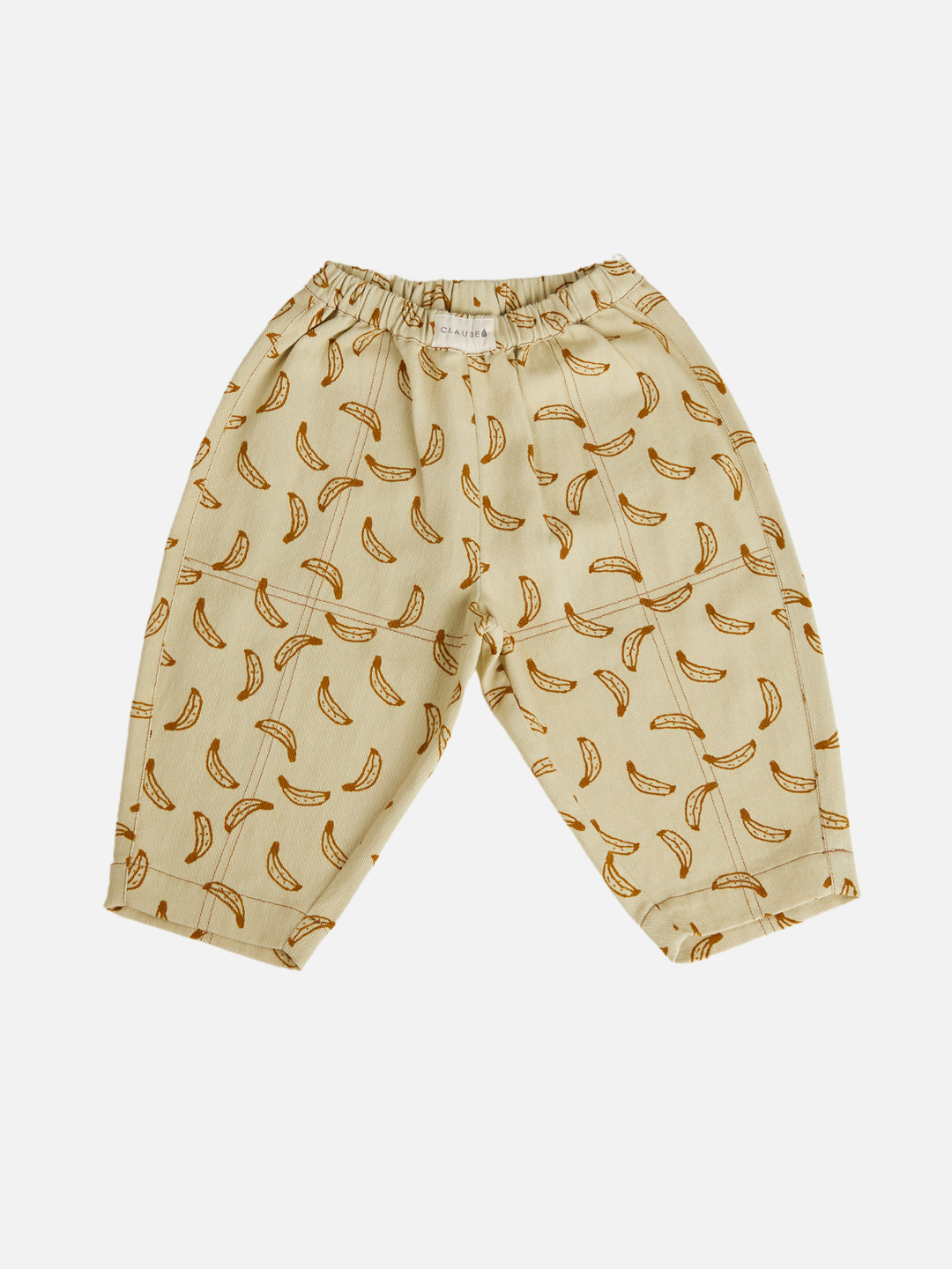 The RIAN BANANA TROUSER is a beige unisex pant made from organic cotton twill with an elastic waistband and playful repeating banana print, featuring oversized balloon legs and shown laid flat on a white background.