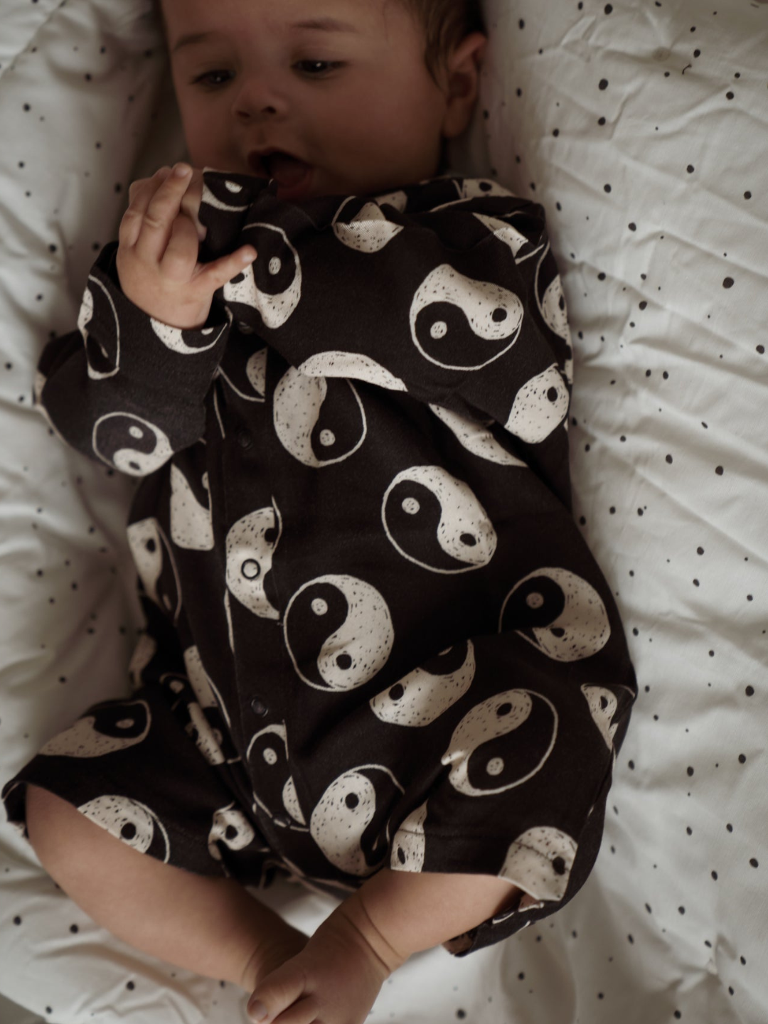 A front view of the roomy jumpsuit on a baby. Black with a yin and yang pattern all over. Front snap button closure.