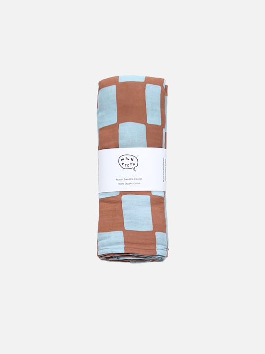 Image of Blue Checkers | A MUSLIN SWADDLE BLANKET in a blue checkers print, made of 100% organic cotton, folded and wrapped with a white label that says “Mush Swaddle Blanket.”.