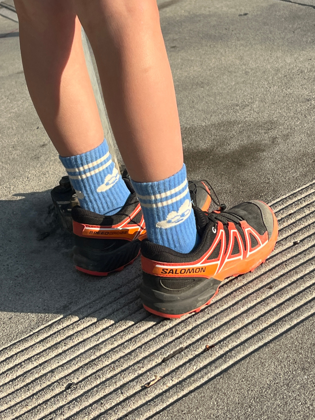 Cloud | Person wearing blue socks with white stripes and Salomon running shoes on a pavement.