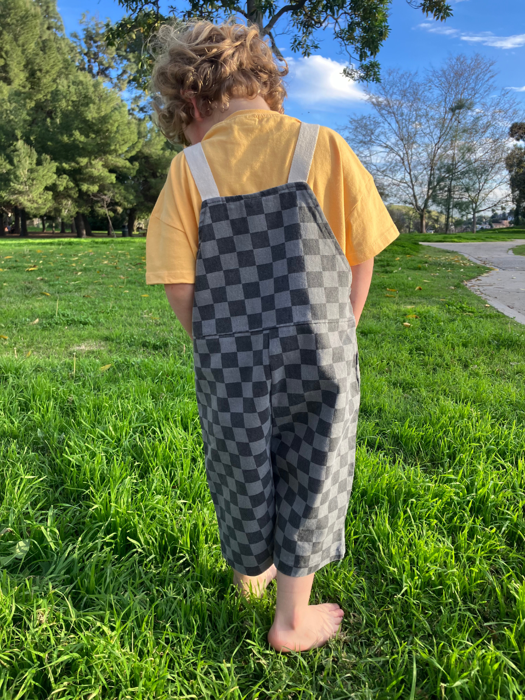 A child is wearing checker overalls in charcoal over a yellow tee