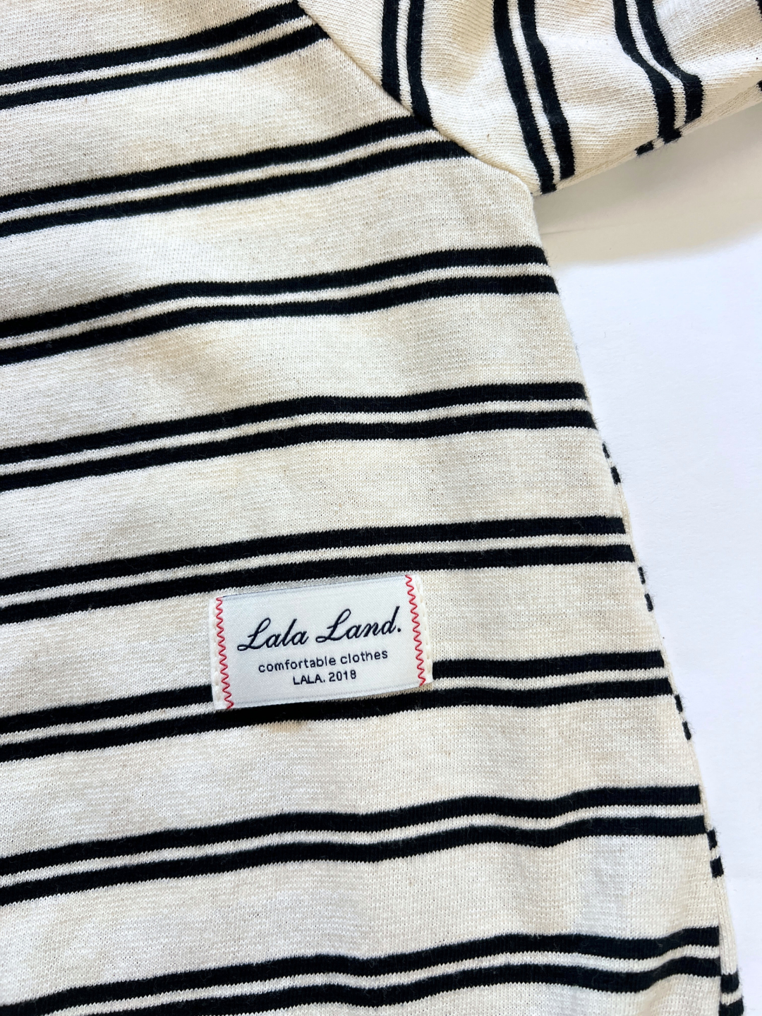 The SLOUCHY STRIPE ROMPER is a cream cotton jersey romper with black horizontal stripes, finished with a white “Lala Land. comfortable clothes LALA.2018” label near the hem, inspired by trendy Korean baby brands.