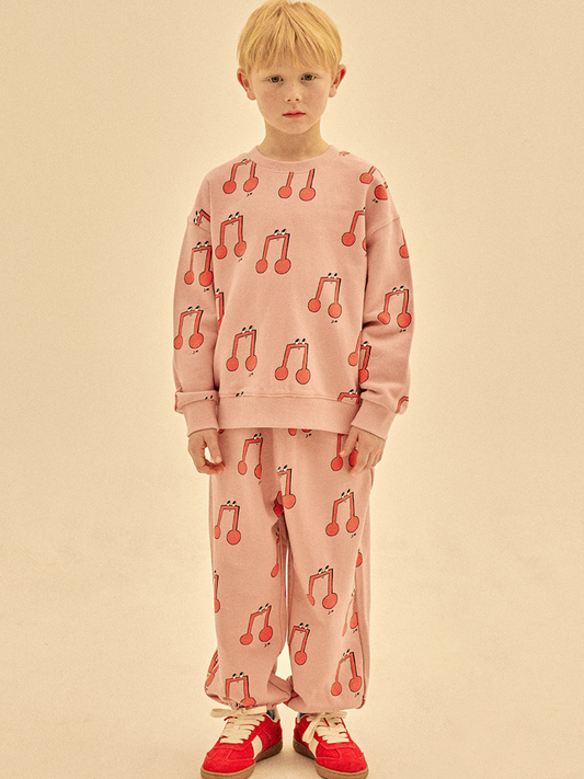 Second image of The MELODY PATTERN SWEATSHIRT is a pink children's sweatshirt with a lively red musical note pattern featuring smiling faces on white, delivering cheerful style at an affordable price.
