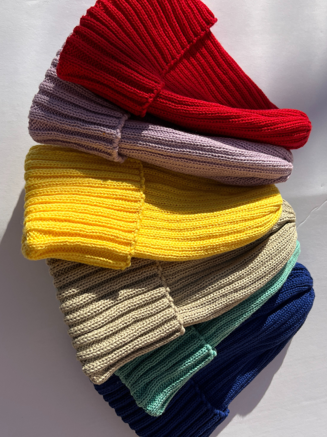 Khaki | Group of lilac, red, khaki, blue, mint and yellow baby beanies on a white background.