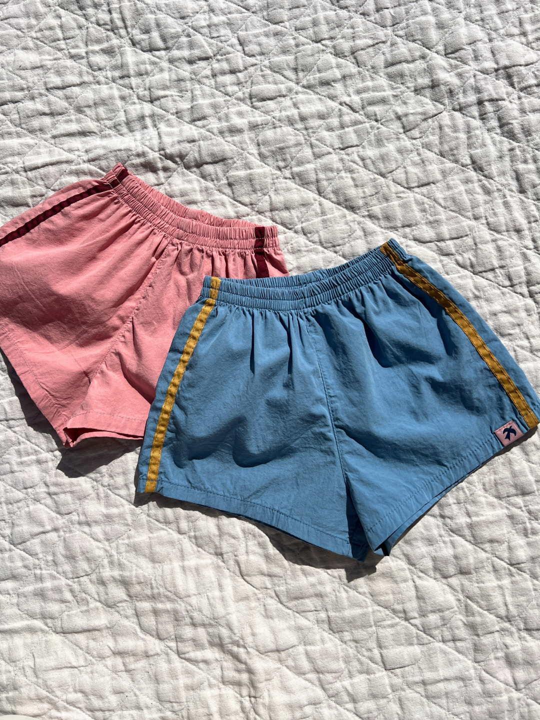 Dusty Pink | Both colors of the track shorts laid flat on a quilt outside. 