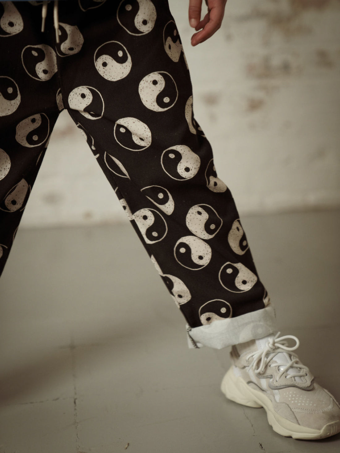 A zoomed in front view of the drawstring black pants with a yin and yang pattern all over on a child with the ankles cuffed.