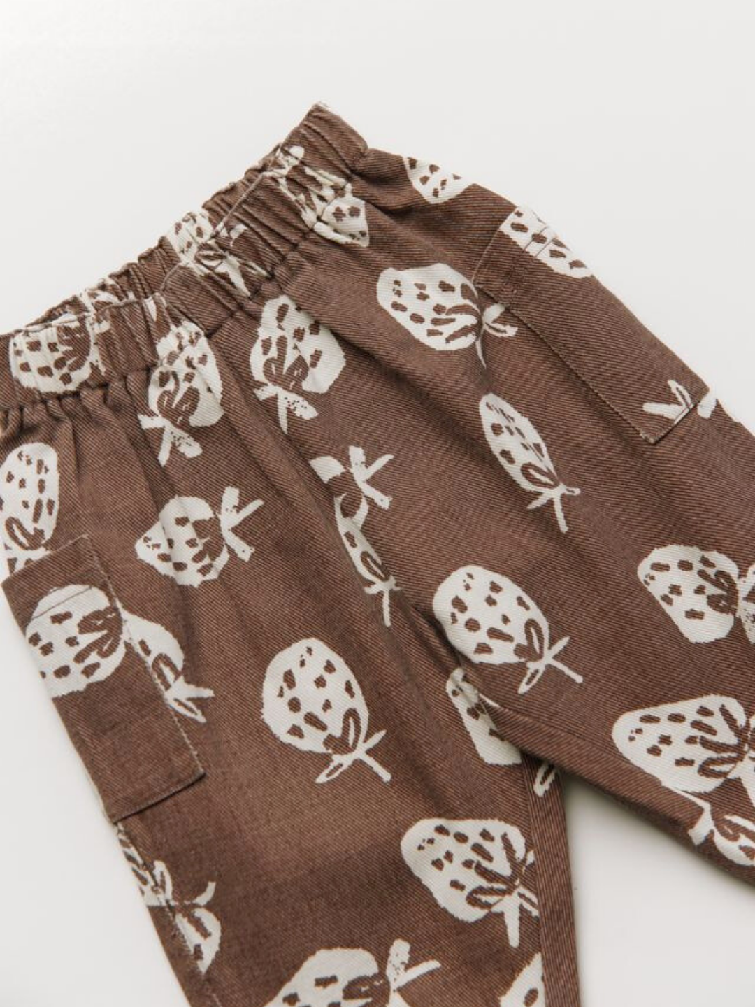 The EMERSON CHOC STRAB TROUSER features an elastic waistband, white strawberry print, and side pockets, shown on a white background.