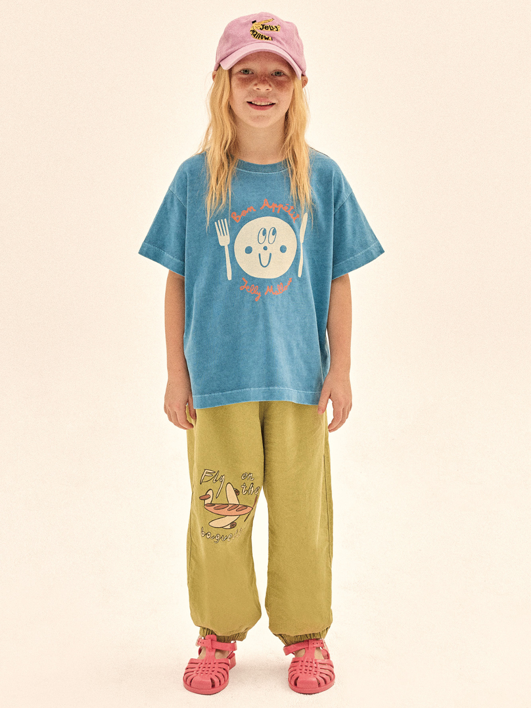 Child wearing a blue t-shirt with a smiley face design and yellow pants on a beige background