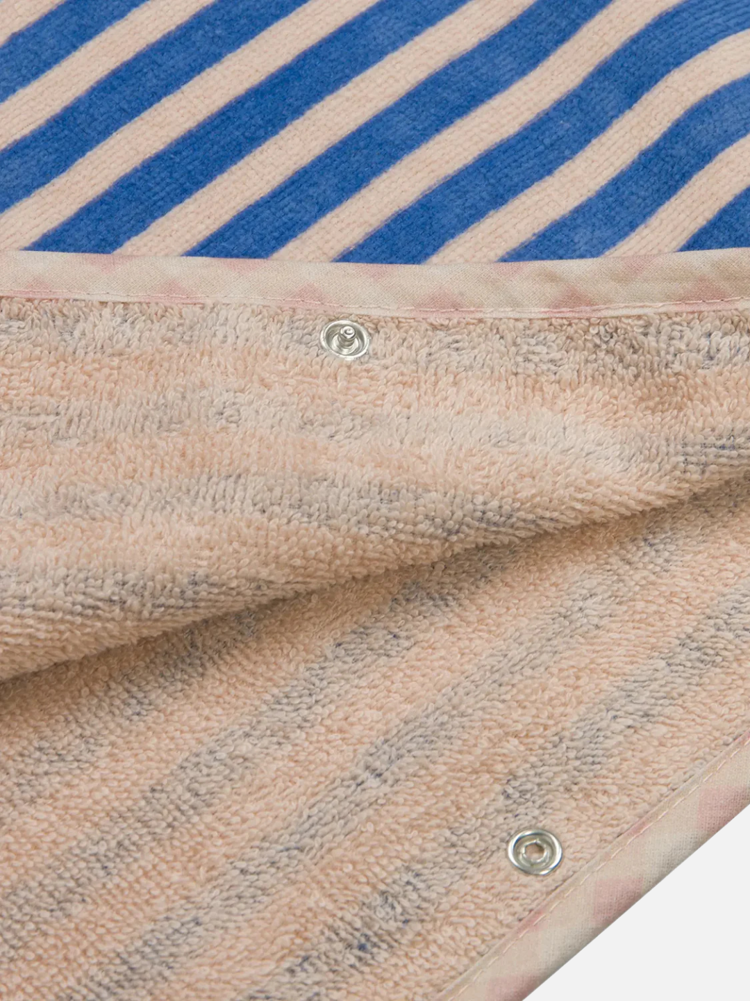 Close-up of the STRIPED PONCHO in blue and beige, featuring textured fabric, detailed stitching, OEKO-TEX certified material, and metal snap buttons along the edge.