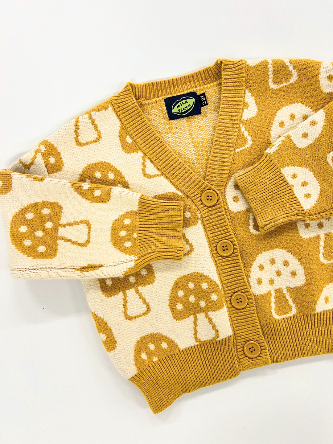 The SHROOM CARDIGAN, featuring an enchanting mushroom pattern in brown and cream, is buttoned up and laid out flat against a white background. For precise measurements, please refer to the detailed description provided.