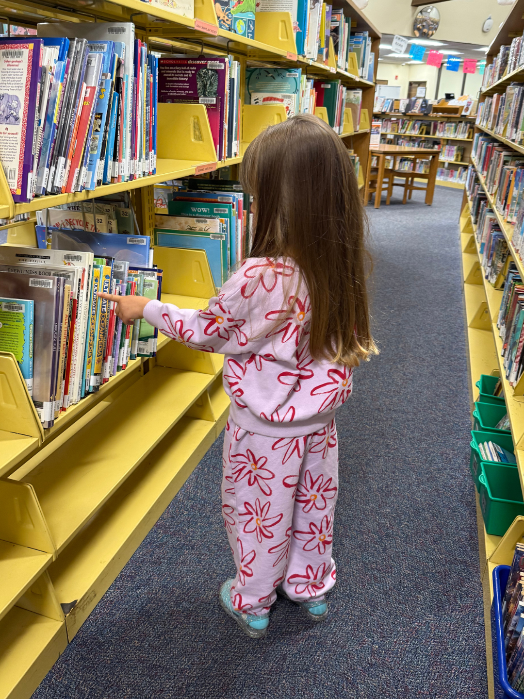 Child in a library reaching for a book on a shelf