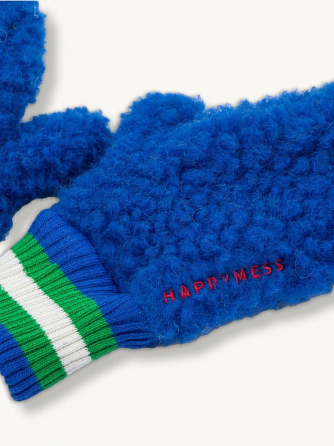 Cobalt | A close-up of the MERINO FLEECE MITTEN shows its blue fuzzy thermal design and green and white striped organic cotton cuff, with "HAPPYMESS" embroidered in red.