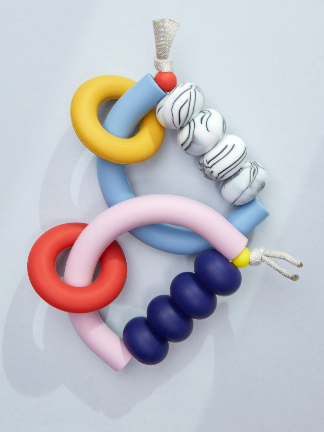 Memphis | Two sensory-friendly MT X JM ARCH RING TEETHERS: one blue/yellow with white marbled beads, one pink/red with navy beads, both displayed on a light gray background. Crafted by a trusted US-made brand.