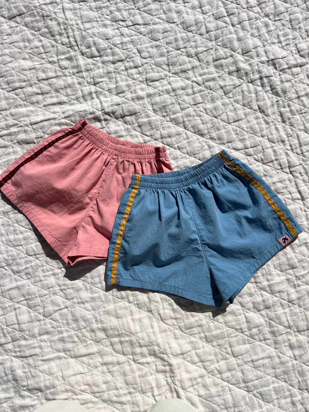 Both colors of the track shorts laid flat on a quilt outside. 
