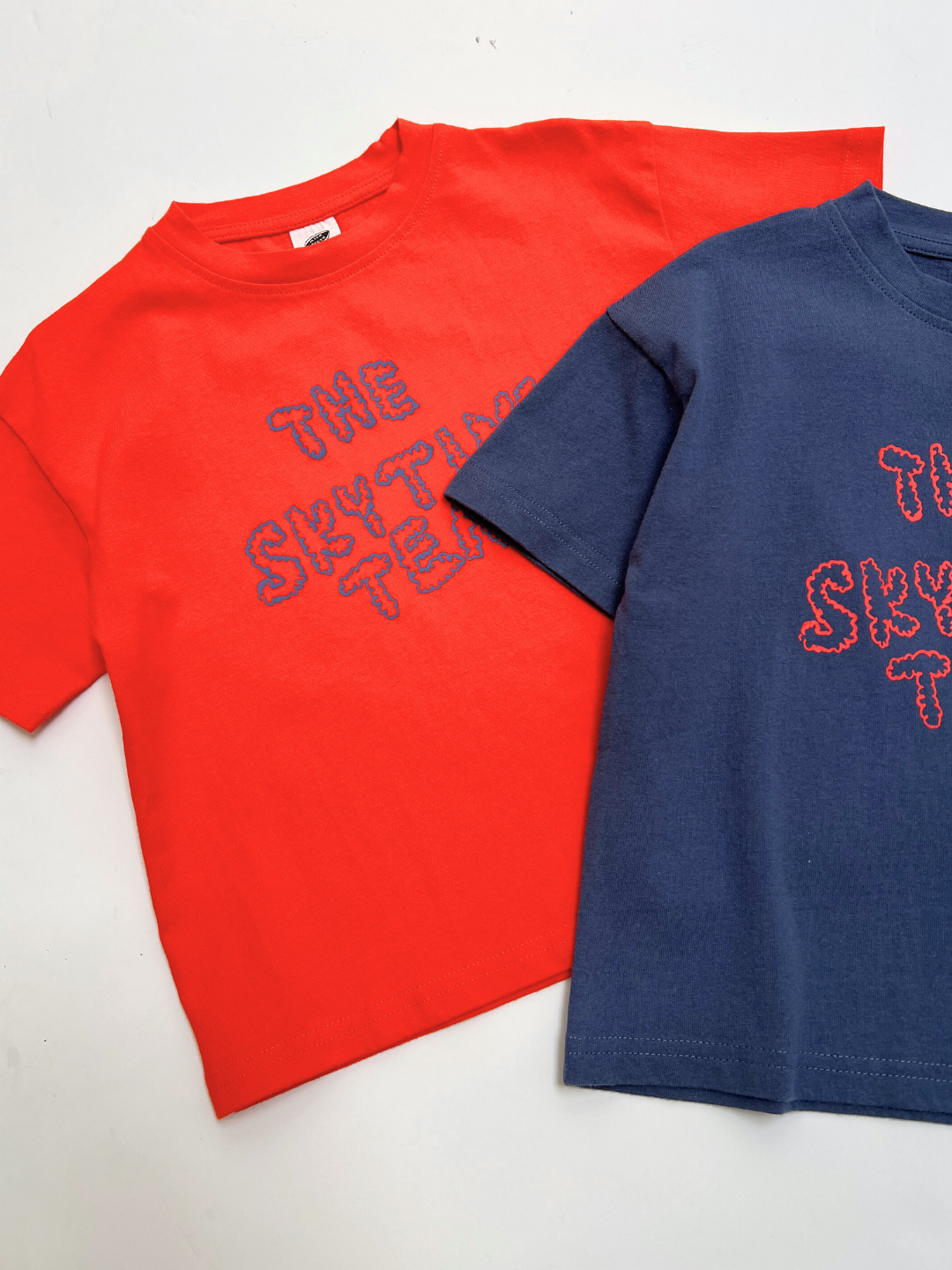 The SKYTIME TEE comes in red and navy blue, each with "THE SKYLINE TEAM" in a textured outline on the front. These oversized, boxy t-shirts deliver cool comfort and standout style with an artist-designed touch.