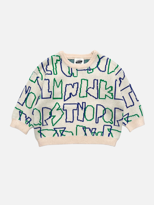 Image of A cream-colored knit kids sweater with a bold, abstract pattern of blue and green alphabet letters, laid flat against a light gray background.