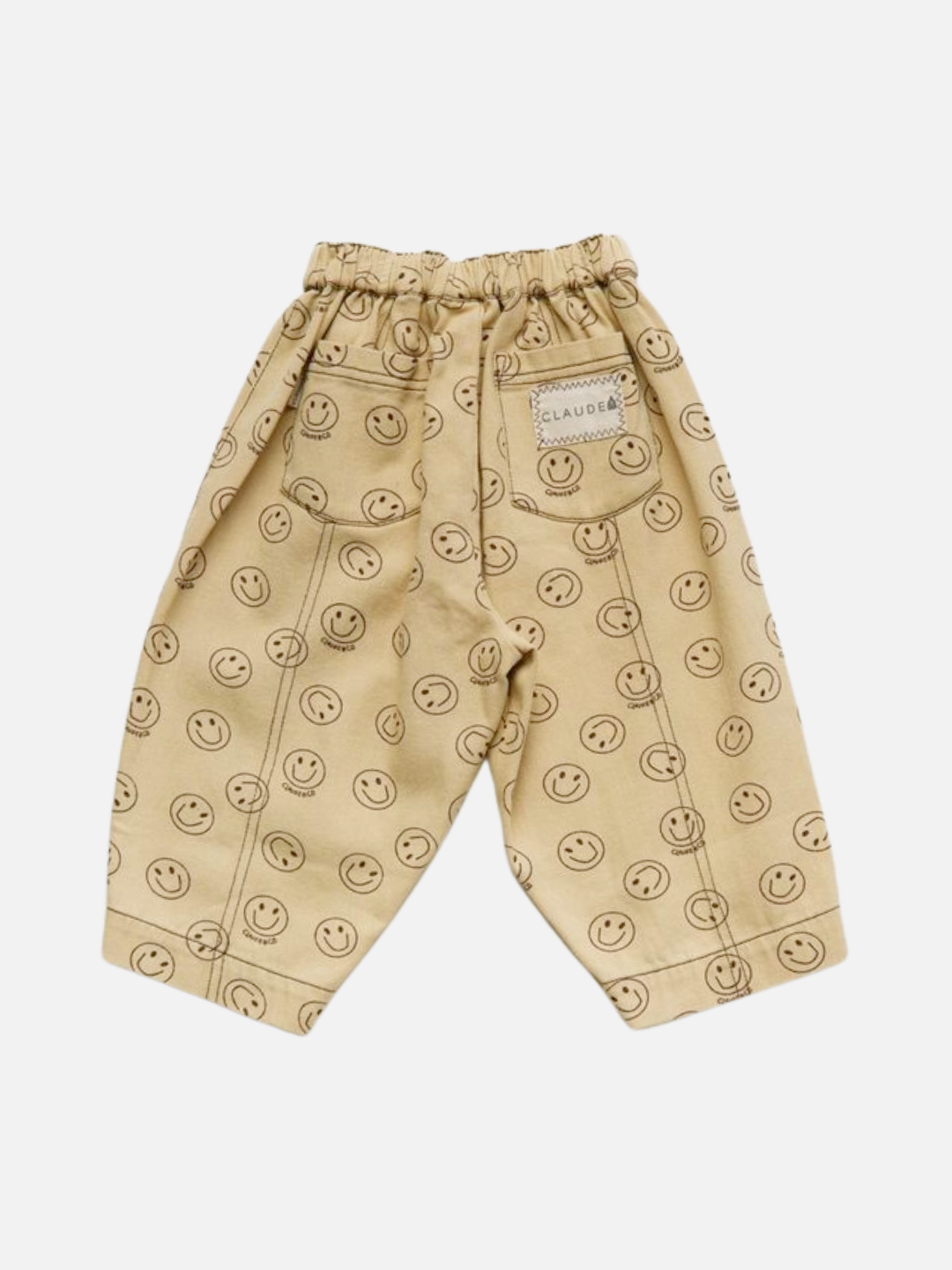 REX JOY BUTTER TROUSER: Beige children's pants with an elastic waistband, all-over black smiley face print, and a label on one back pocket, shown on a white background.