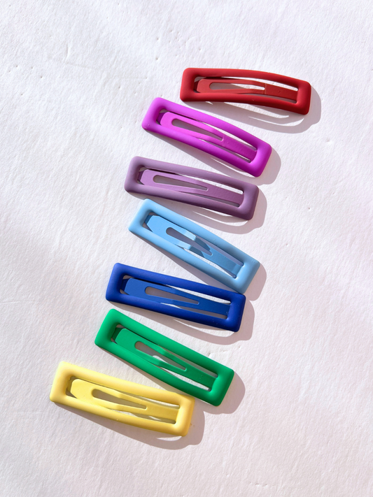 Image of Seven vibrant jumbo rainbow snap clips are arranged in a vertical line on a white background, exuding a cheerful aura that reflects the playful style of Eugenia Kids.