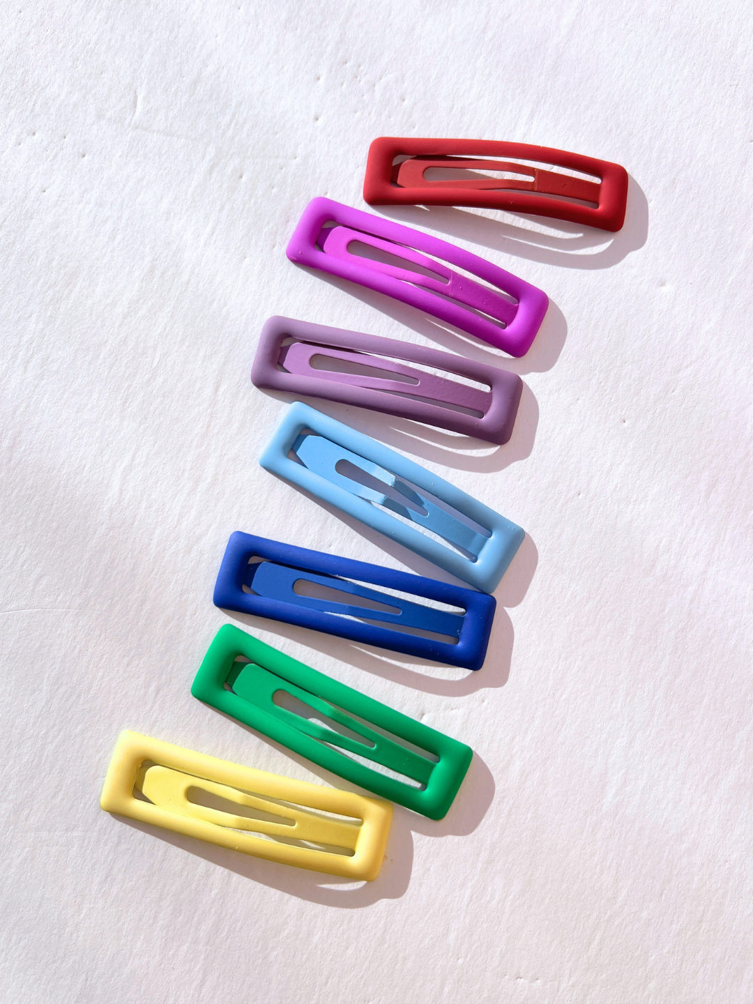 Seven vibrant jumbo rainbow snap clips are arranged in a vertical line on a white background, exuding a cheerful aura that reflects the playful style of Eugenia Kids.