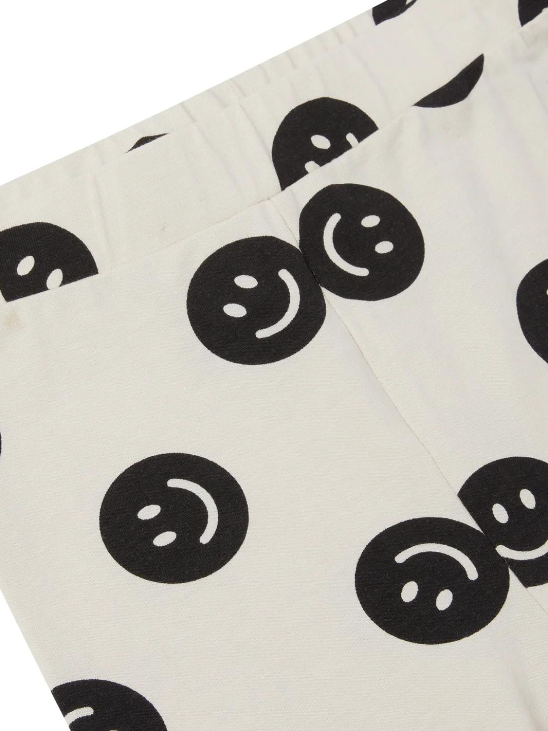 A zoomed in front view of the cream colored leggings with a black smiley face pattern.