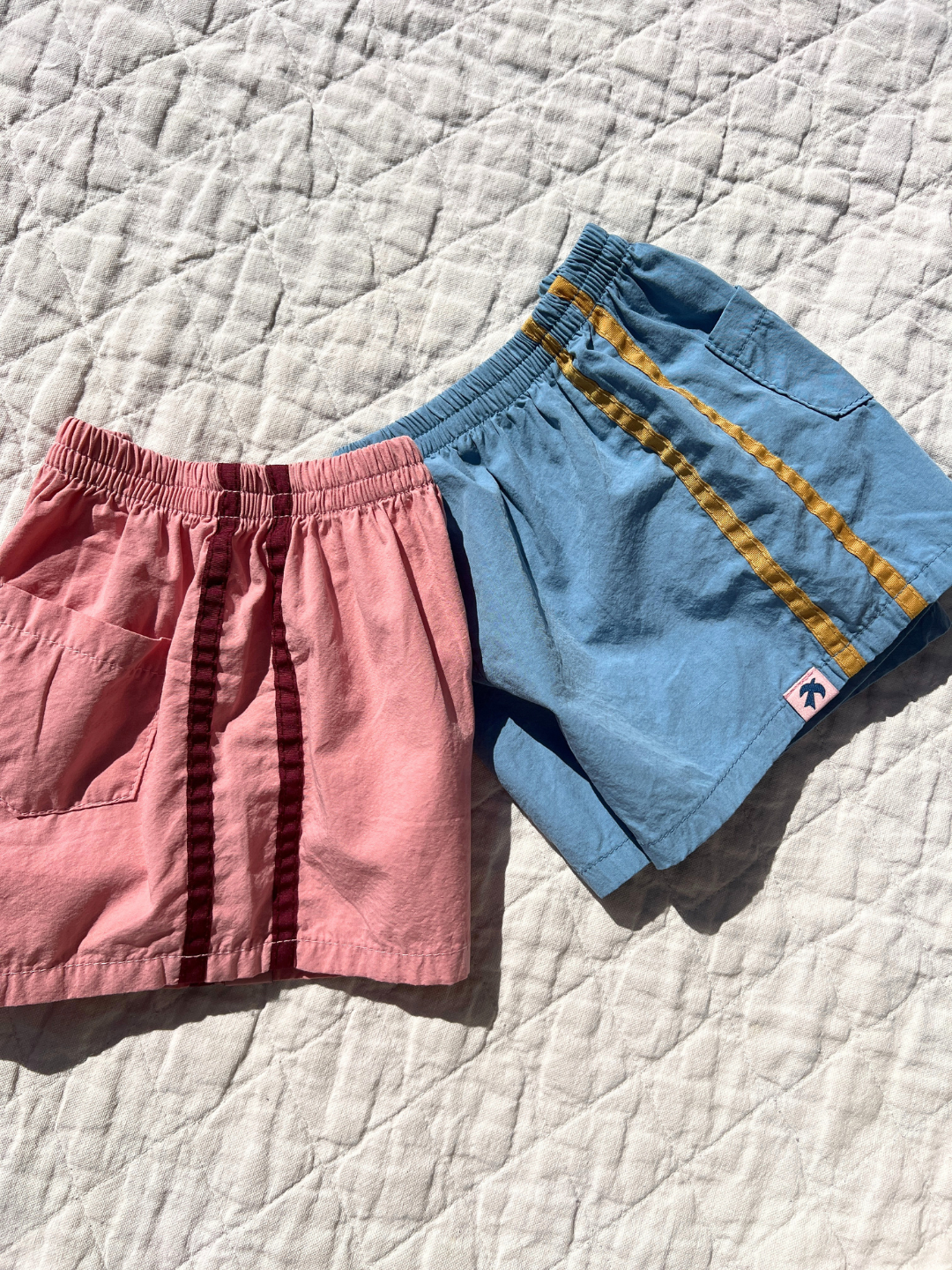 Sky Blue | Both colors of the track shorts laid flat on a quilt outside. 