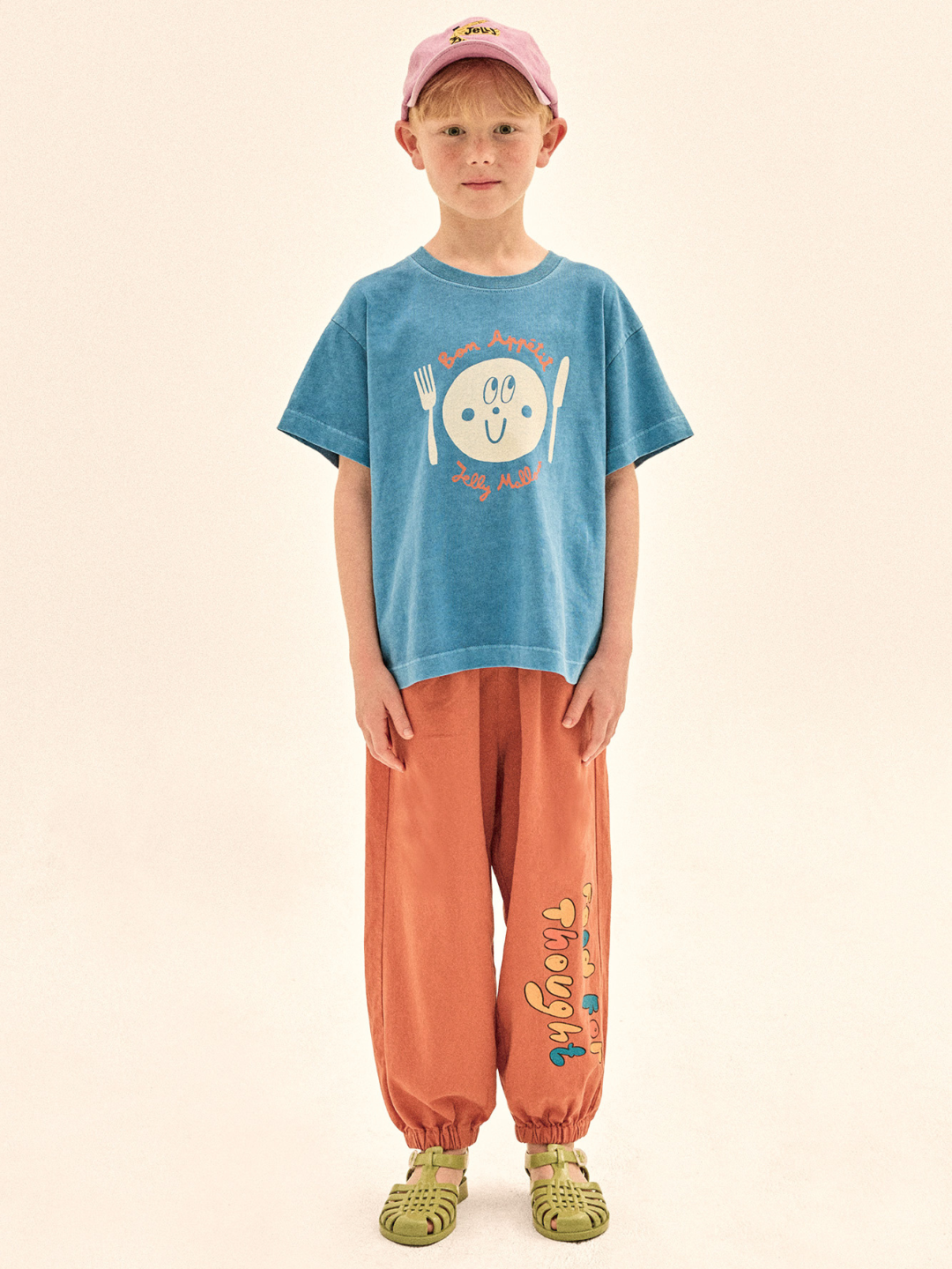 Child wearing a blue t-shirt with a graphic design and orange pants on a beige background