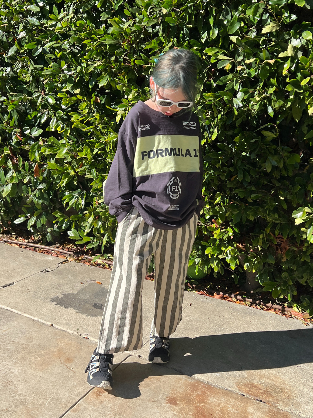 Person wearing a 'Formula 1' sweatshirt standing in front of green bushes.