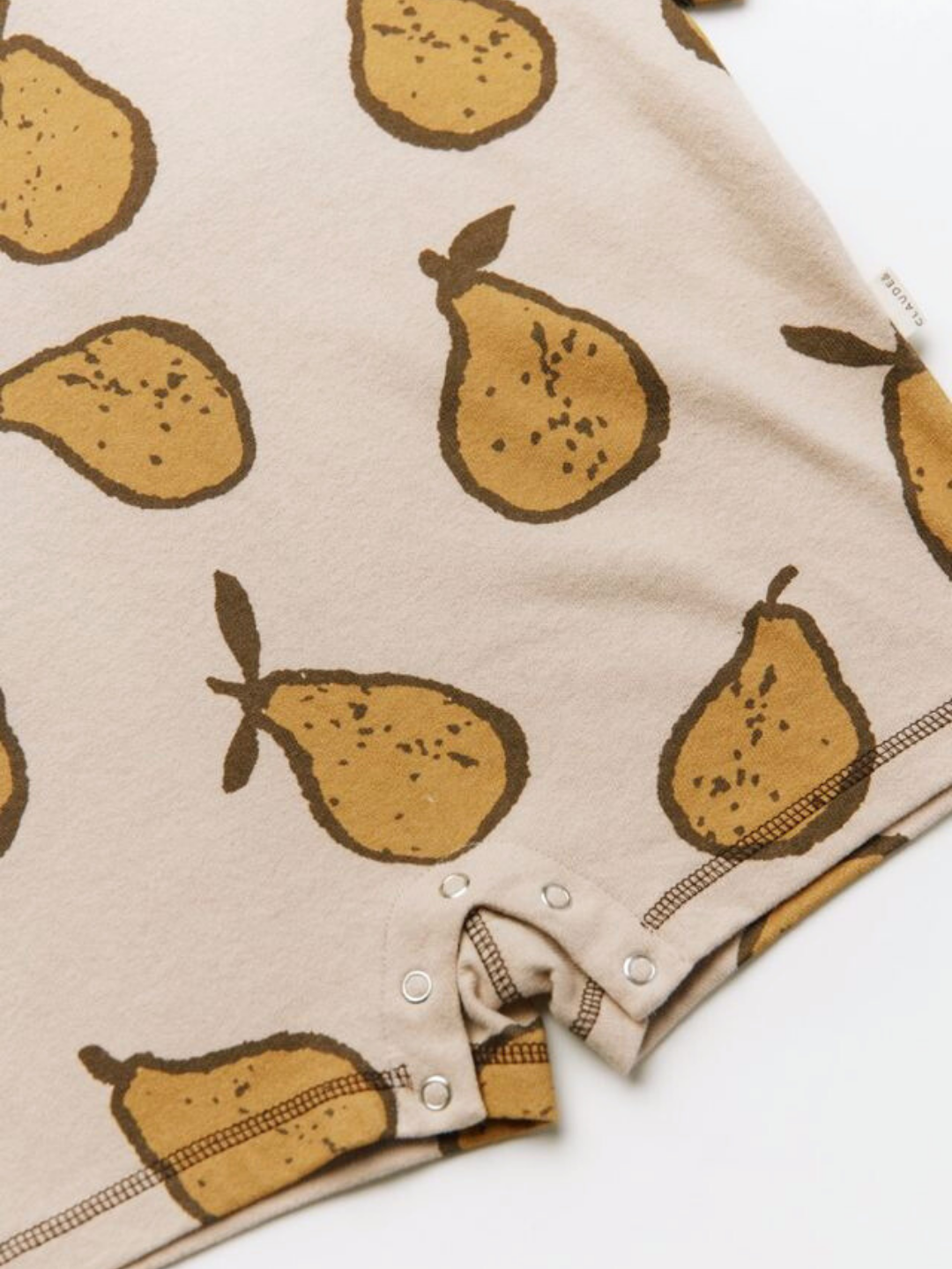 The OPAL ALMOND PEAR ROMPER features beige fabric with a pear print and metal snap buttons along the bottom edge.