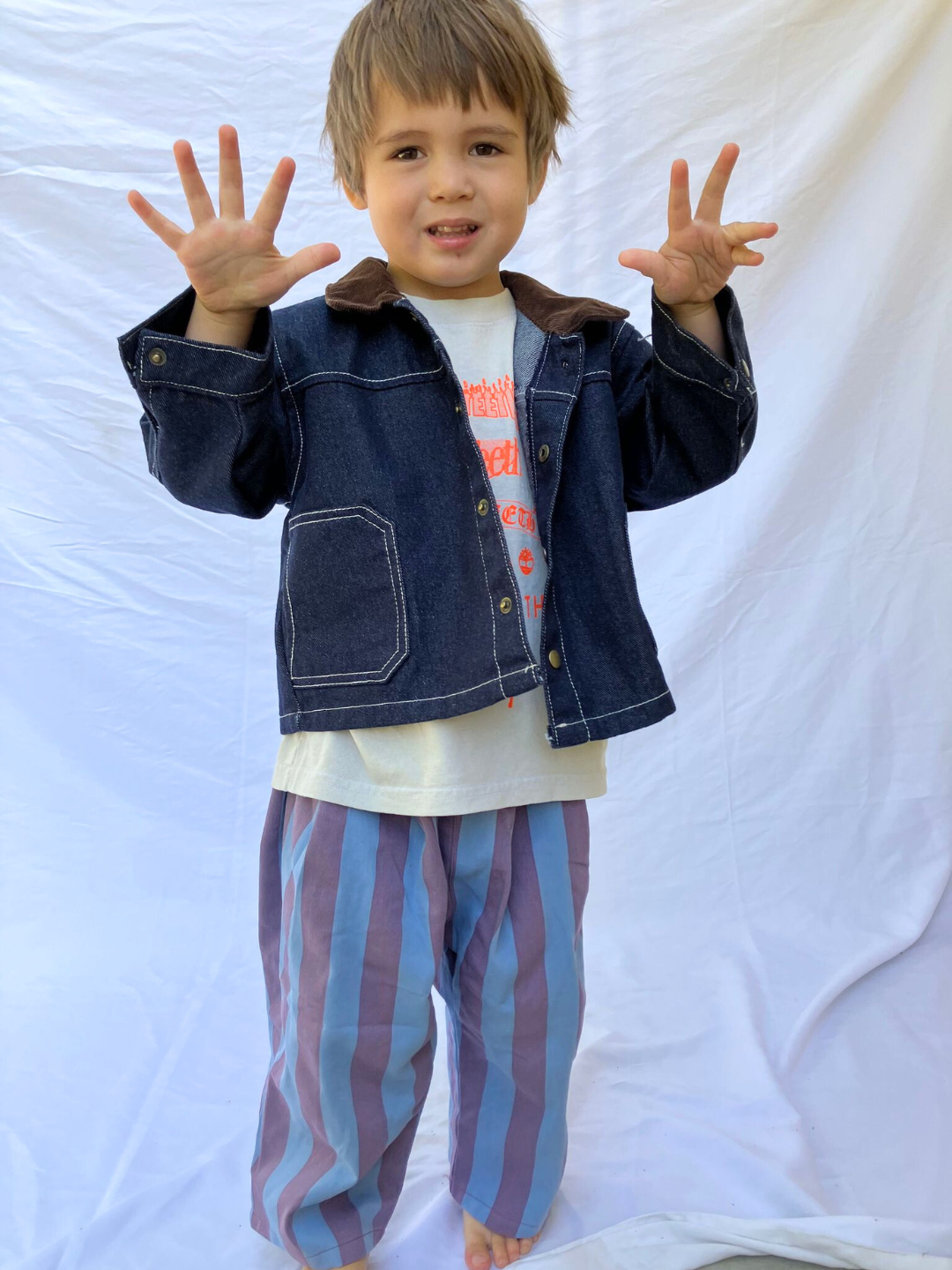 A child wearing Indigo Weekender Jacked, Striped Crayon purple pants, and cement tee. 