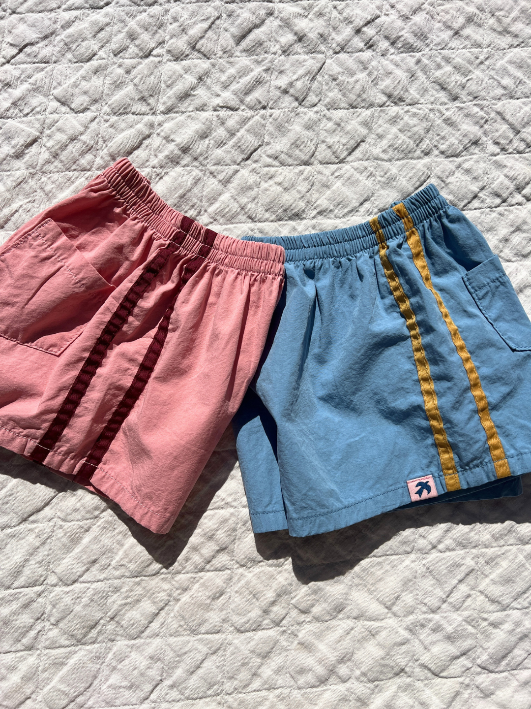Dusty Pink | Both colors of the track shorts laid flat on a quilt outside. 