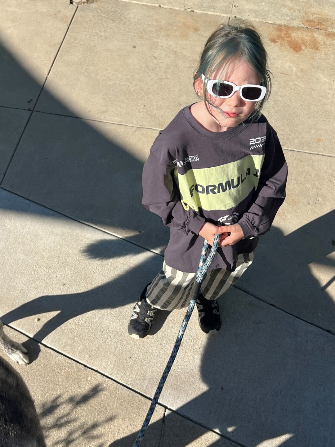 Child wearing sunglasses and a long-sleeve shirt with 'Formula' on a sidewalk