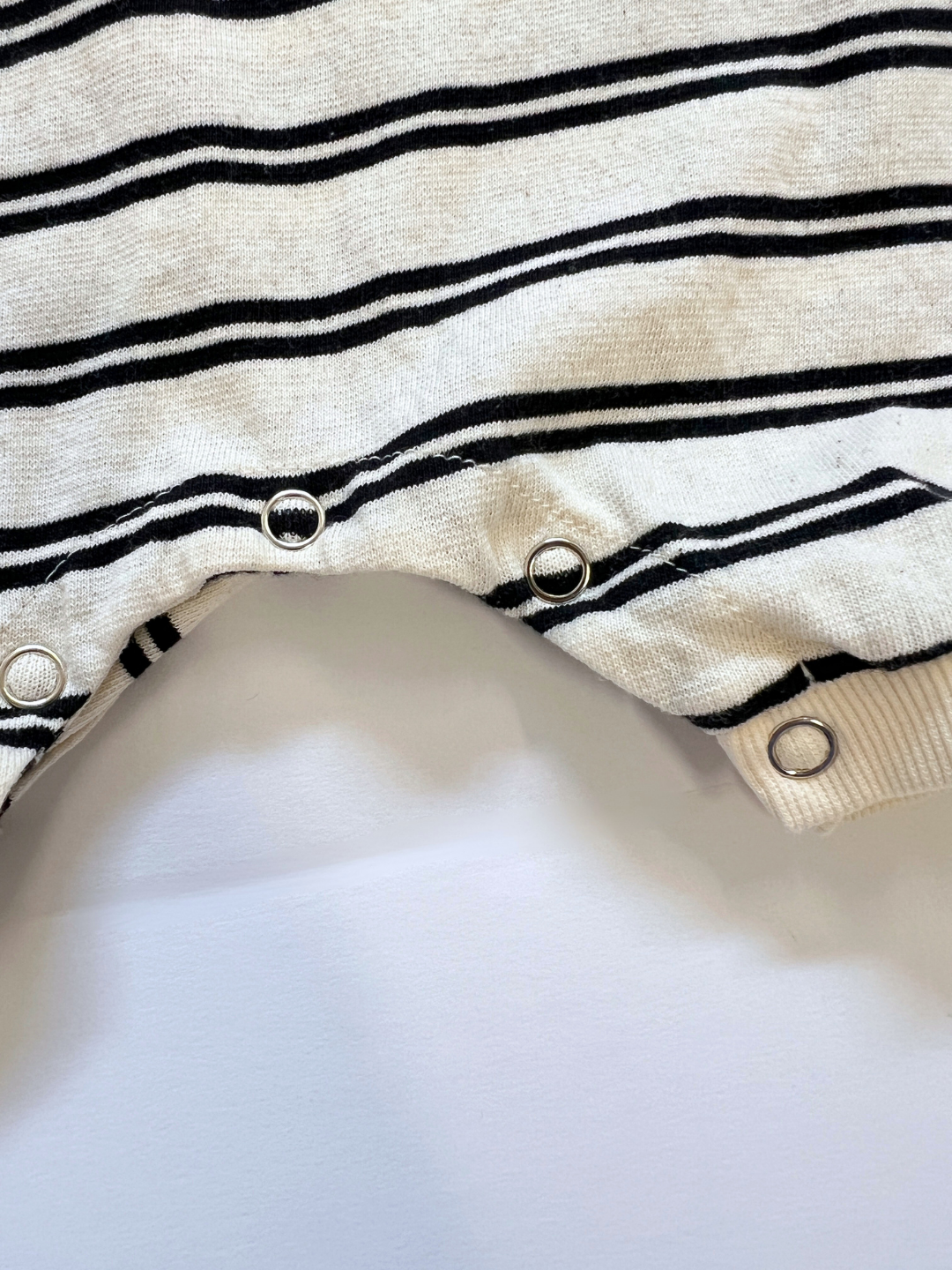 Off-White | Close-up of the SLOUCHY STRIPE ROMPER, a soft cotton jersey shortie romper with stripes and three metal snap buttons along the hem, shown on a white background. Designed by a Korean baby brand.
