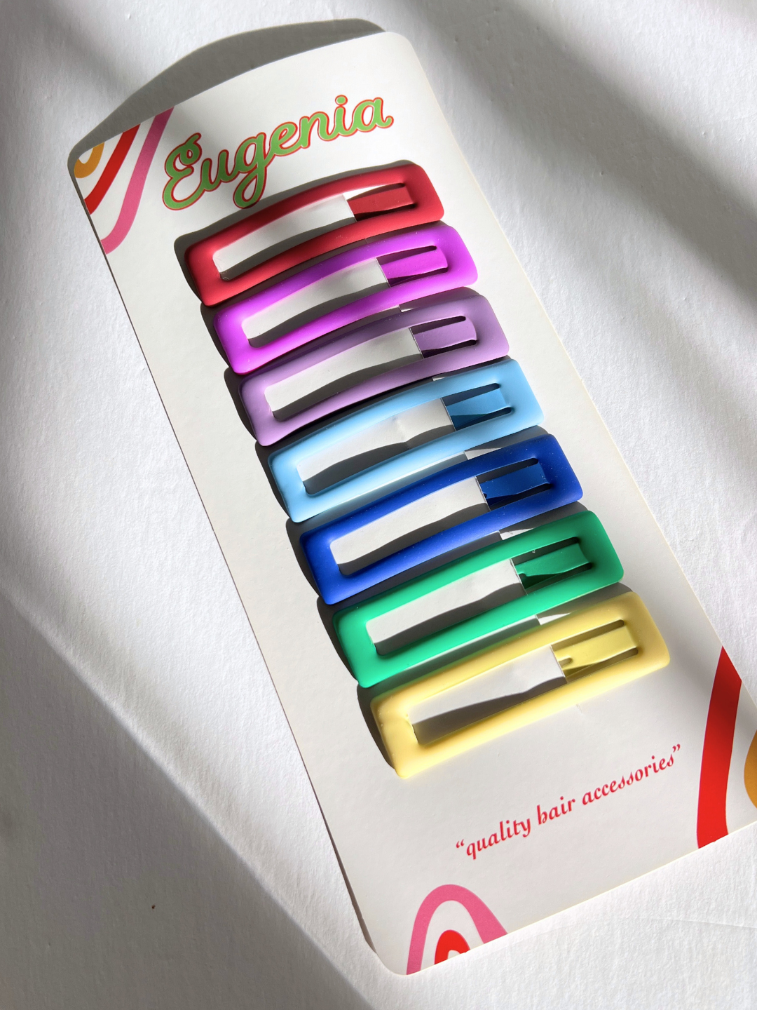 A card of "JUMBO RAINBOW SNAP CLIPS" includes eight large rectangle snap hair clips in pink, purple, blue, green, and yellow with the brand "Eugenia Kids" and the phrase "quality hair accessories.