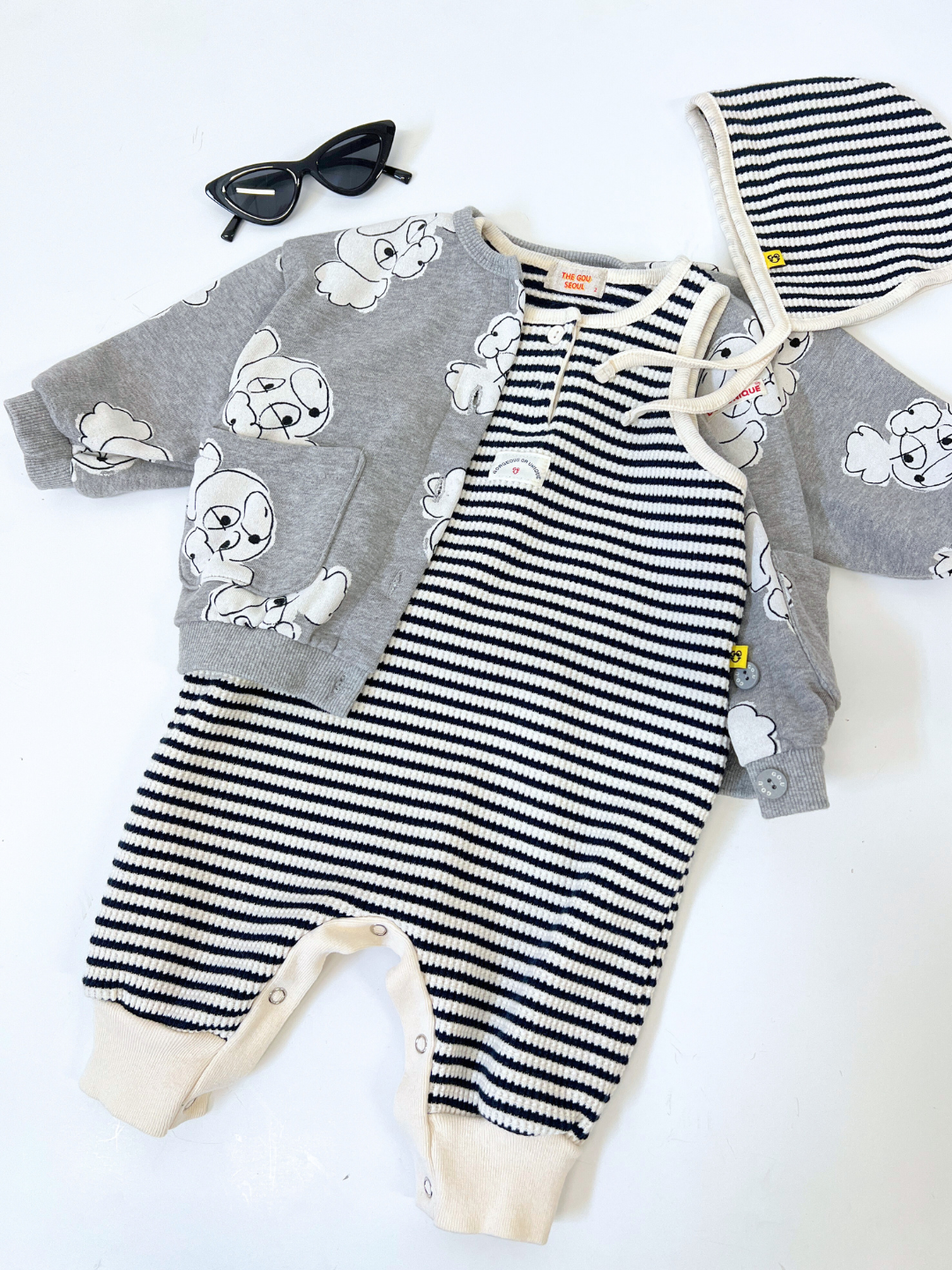 Grey | Charming toddler ensemble with a striped jumpsuit, gray jacket adorned with cartoon clouds, an extra warm baby cardigan, matching bonnet, and classic black sunglasses. Includes the POODLE BUTTON DOWN SWEATSHIRT for added style.