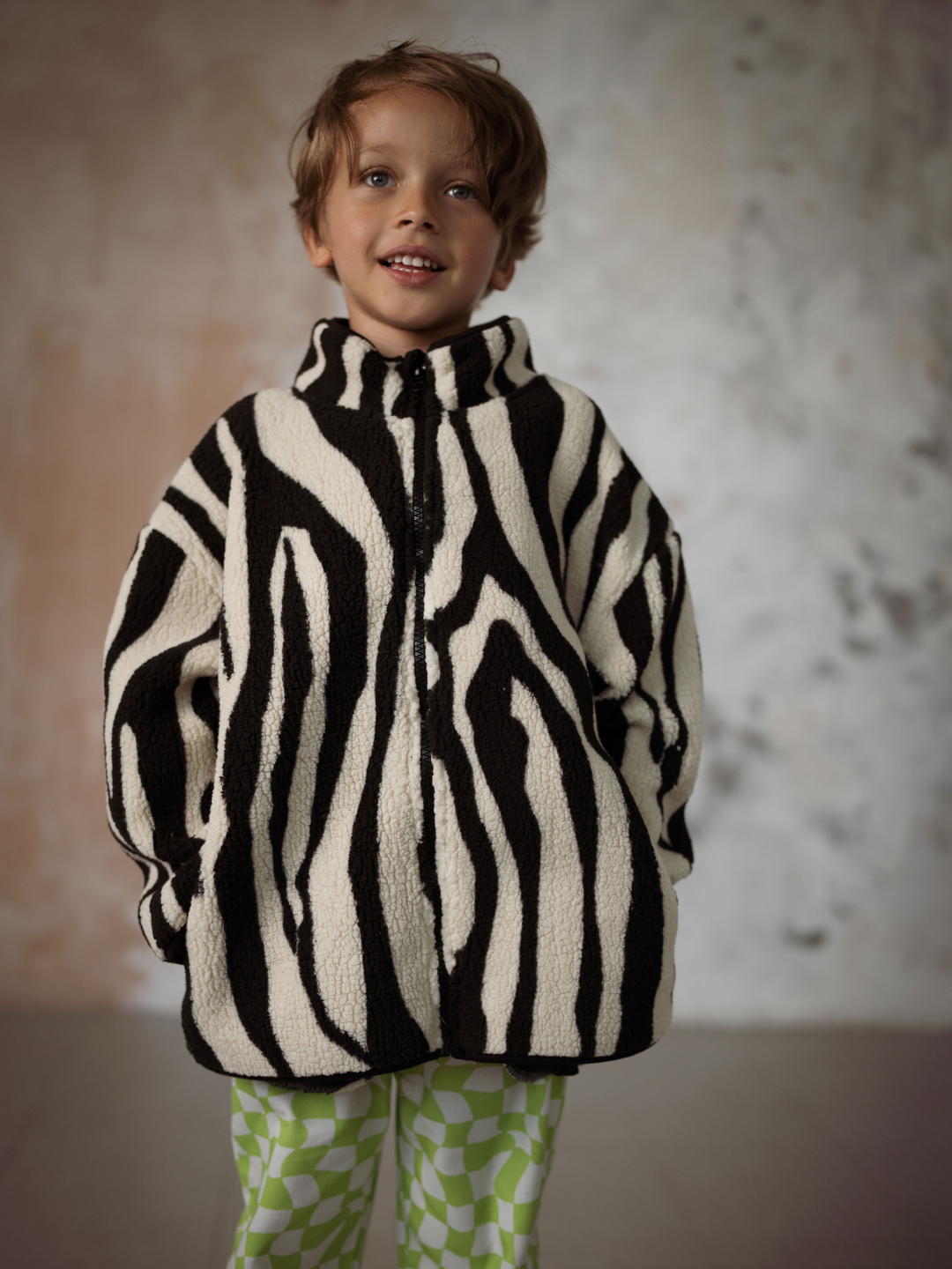 Boy wearing a kids fleece jacket in a black and white tiger stripe pattern.