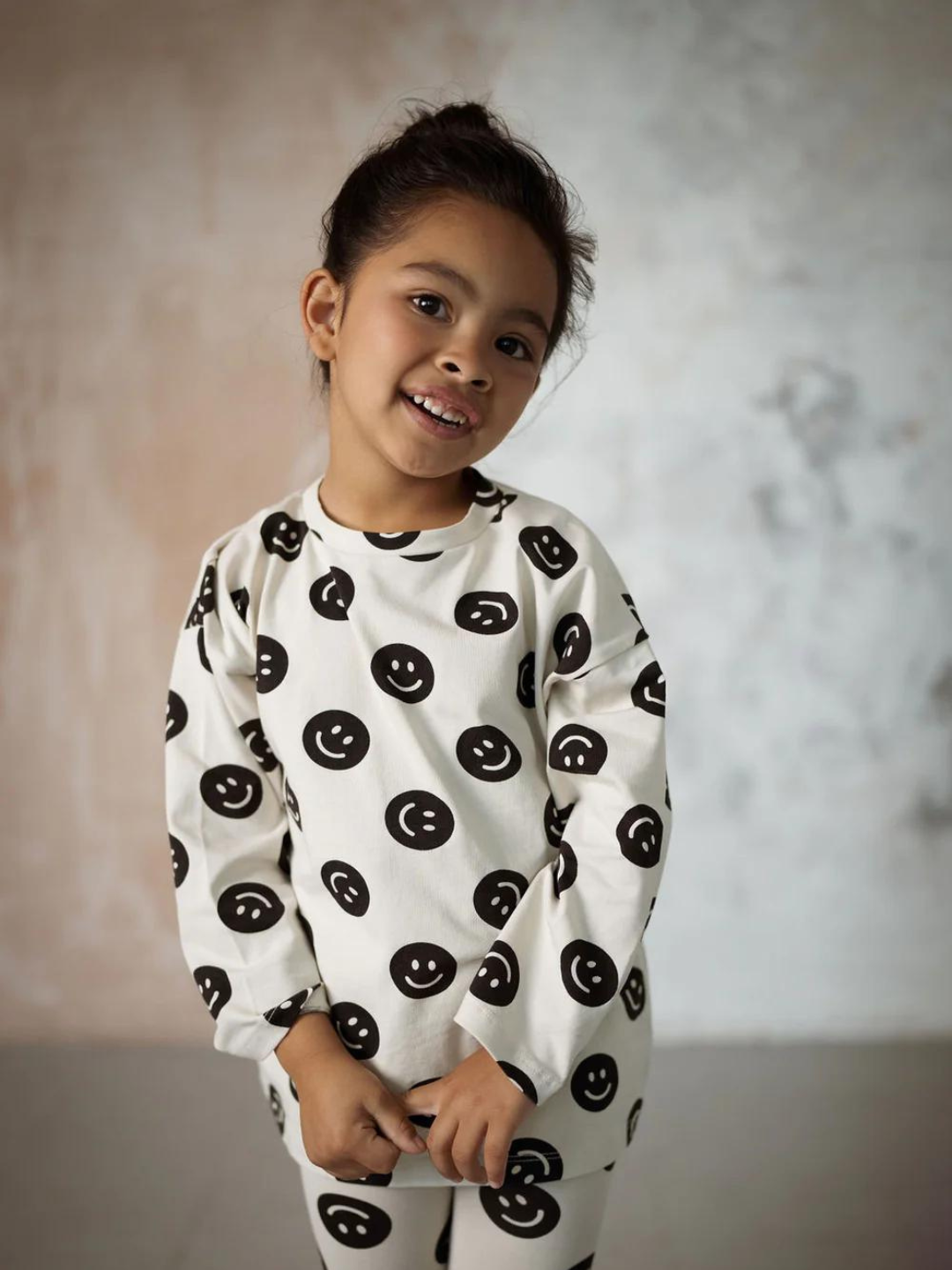 A front view of the cream colored, long sleeve shirt with a black smiley face pattern on a child.