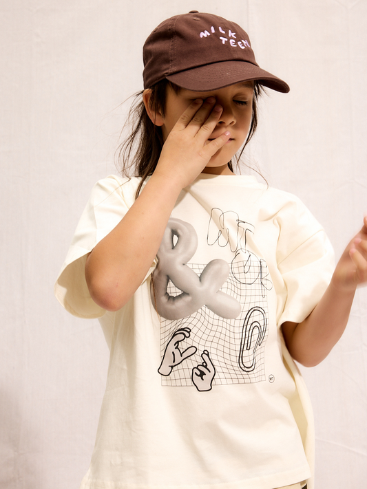 Second image of The CLIP ART TEE is a white short-sleeve shirt made from silky cotton, featuring a graphic ampersand and abstract lines on the front—a fresh addition to your Milk Teeth tee collection.